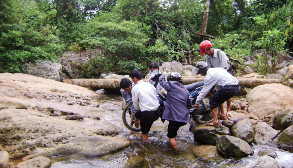 men help carry motorcycle across stream